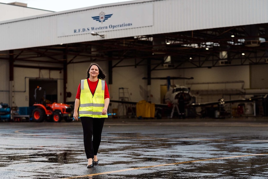 RFDS chief executive Rebecca Tomkinson walks towards the camera away from a hanger wearing a hi-vis vest at Jandakot Airport.
