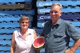 A couple stand in front of pallets holding a watermelon