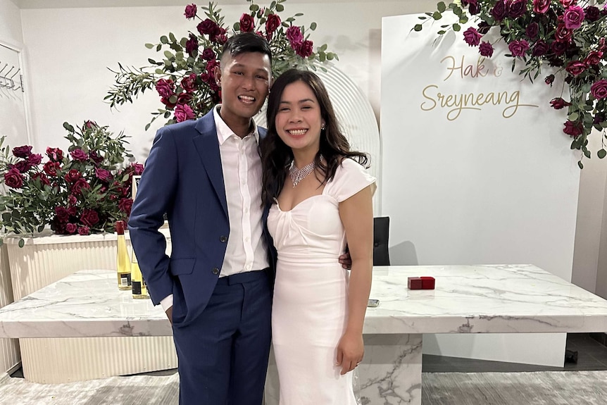 A couple pose on their wedding day beside an arbour with red roses. 