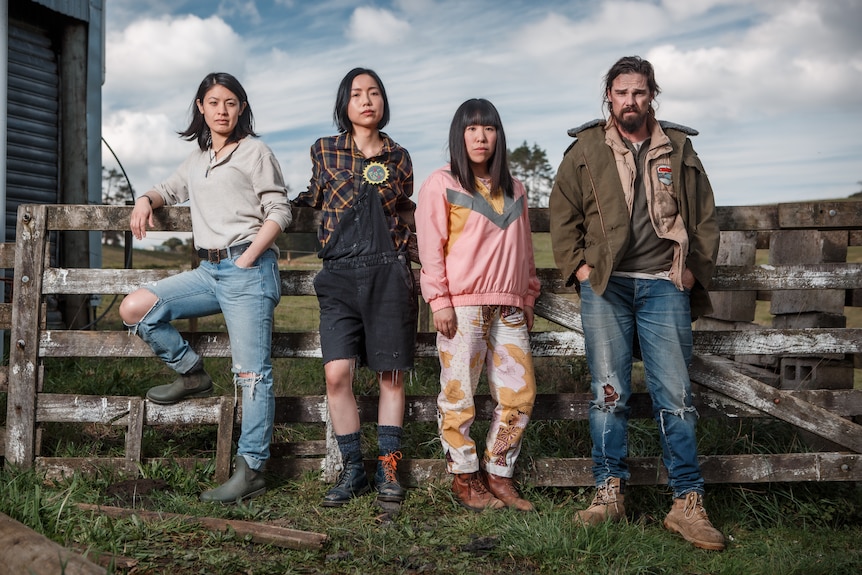 Three Asian women and a white man stand in a row/lean on a farm fence