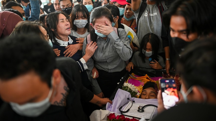 A group of Asian mourners sit in a funeral setting.