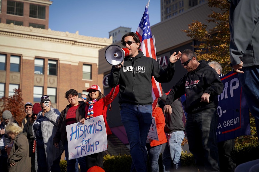 A man in a hoodie that reads #Unsilent uses a megaphone in front of a US flag