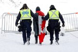 A man with the Canadian flag tied around his neck is led away by two police officers in the snow. 