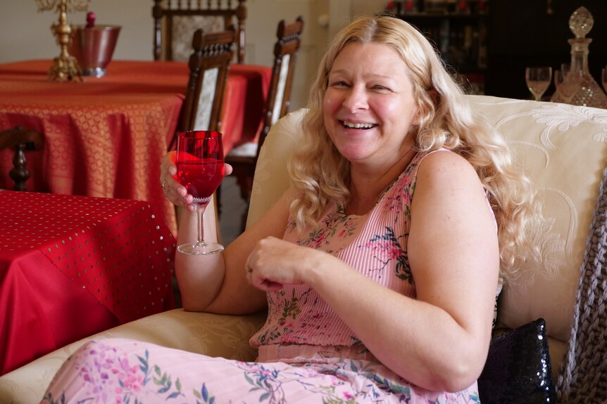 Sasha Gray is sitting on the lounge, enjoying a glass of wine smiling
