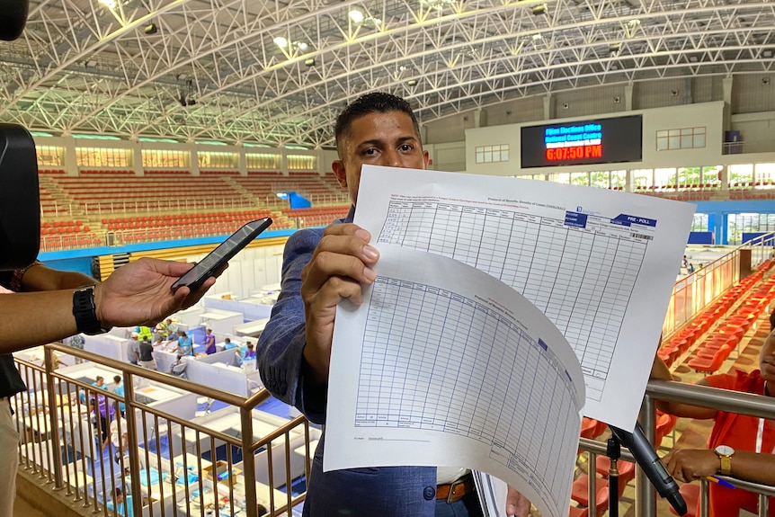 Man holds up two pieces of paper showing election vote results.