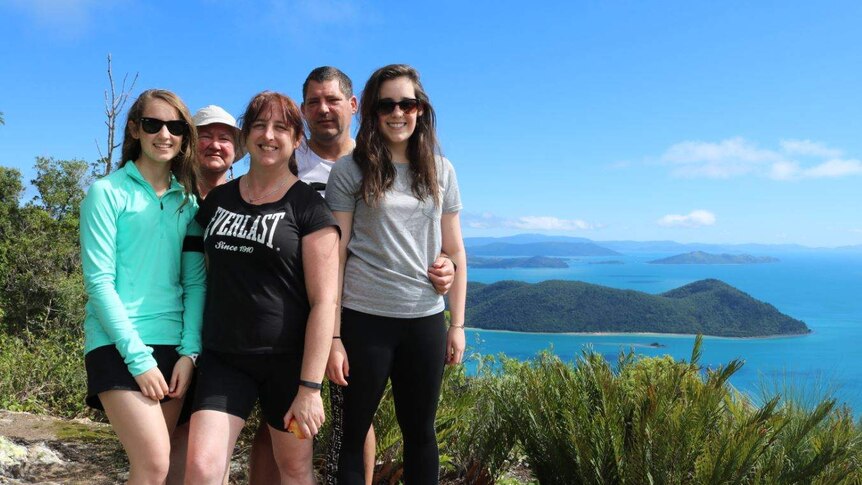 Justine Barwick poses for a group photo with her family. In the background are oceans and islands.