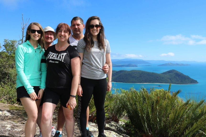 Justine Barwick poses for a group photo with her family. In the background are oceans and islands.