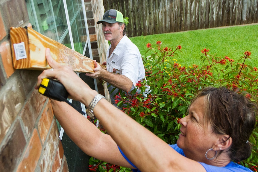 Residents fix a wooden board to the window of their home.