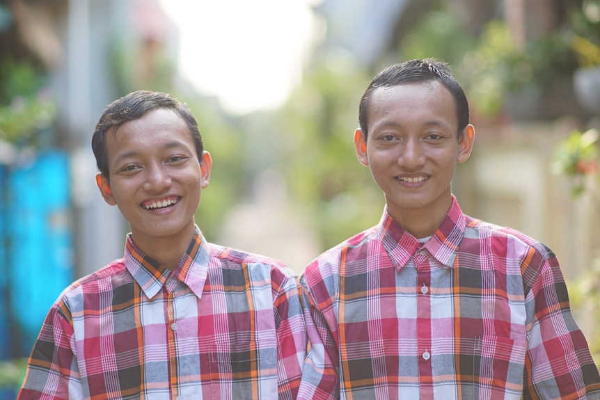 Riky and Riko Prawoto in Indonesia's 'twin village'. They are identical twins and are wearing matching red plaid shirts.