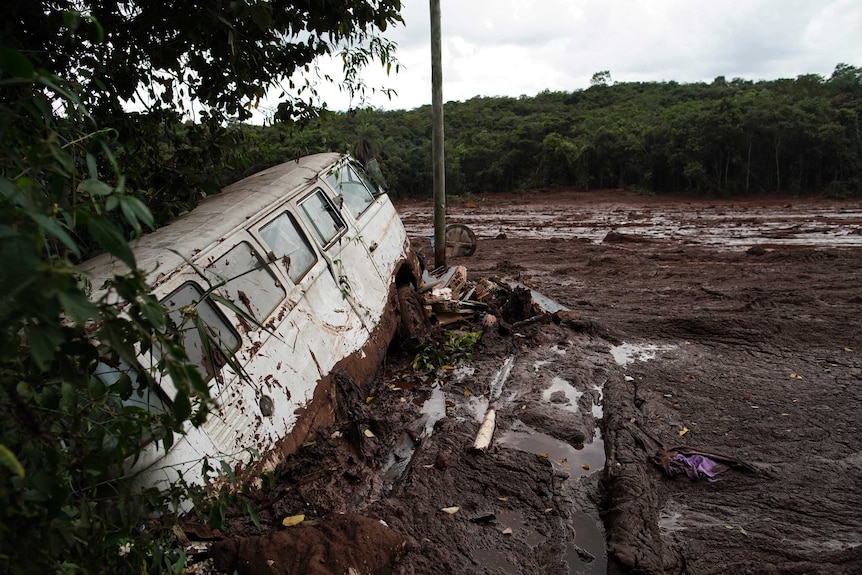 A van half-buried in mud, in front of a sea of mud.