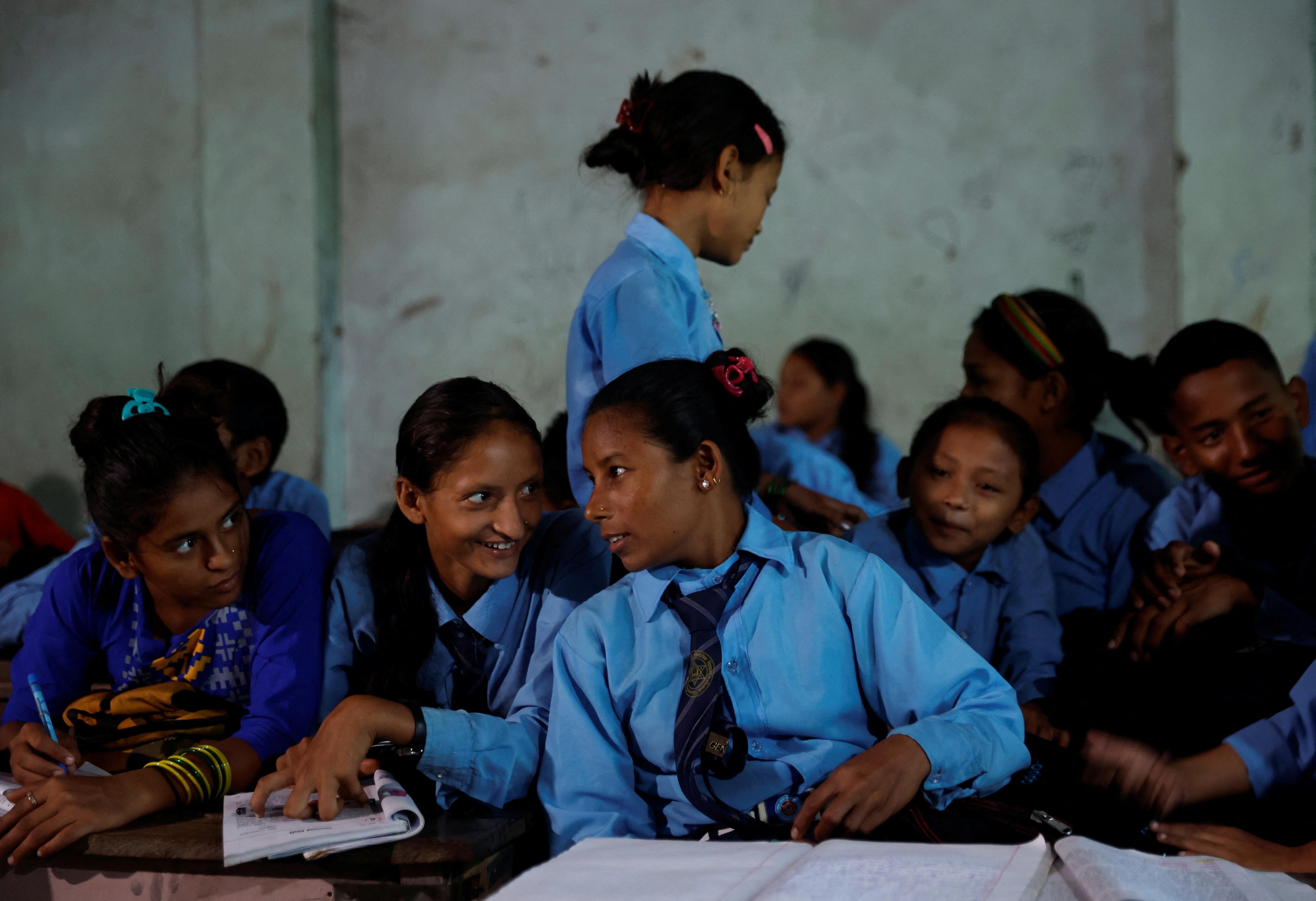 A group of teen girls crowd around an older woman, all wearing the same blue uniform, with schoolbooks in front of them 