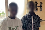A photo of two men standing in a room with their faces blurred.