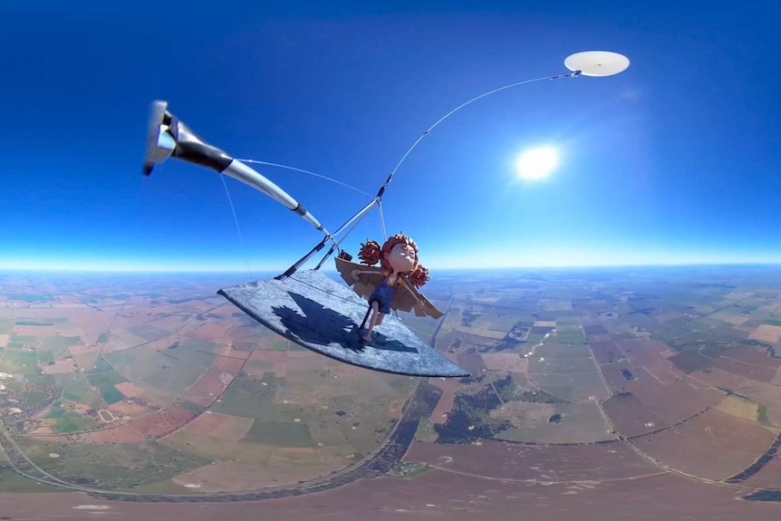 A high-altitude balloon floating carrying a female figurine flying over farmland.