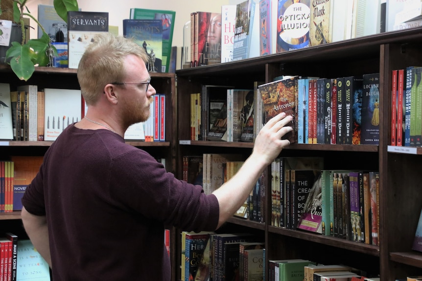 Toby Wools-Cobb carefully pulls out a large old book in his bookstore.