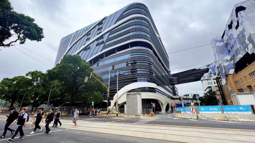 Pedestrians cross the road in front of the Peter MacCallum Cancer Centre