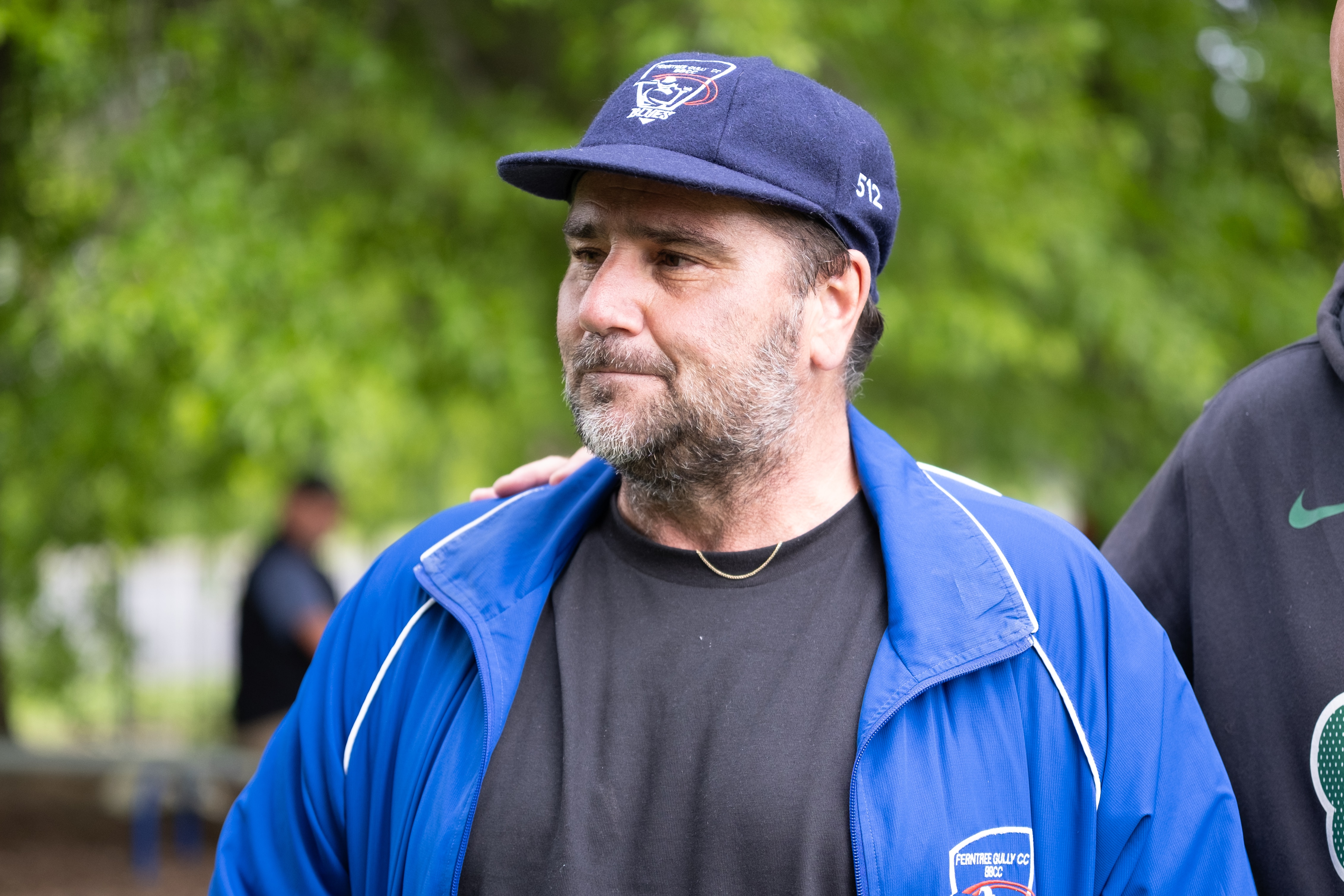 A man wearing a blue jacket and cap looks to the side.