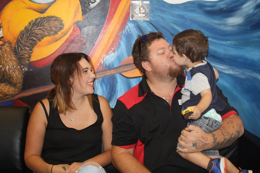 Family of three sits in front of colourful wall