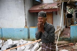 A man stands with his hands over his mouth amidst a damaged village. 