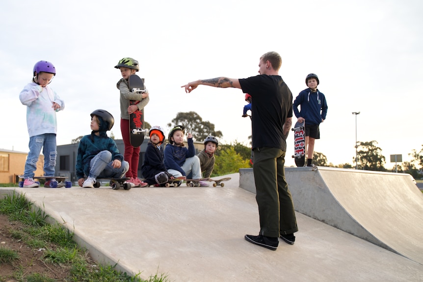 A skating instructor teaches eight kids standing on top of the skate ramp.