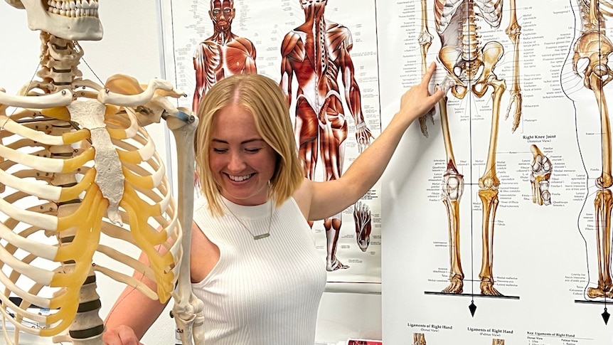 A woman points to a bone on a skeleton model and the corresponding bone on a nearby chart