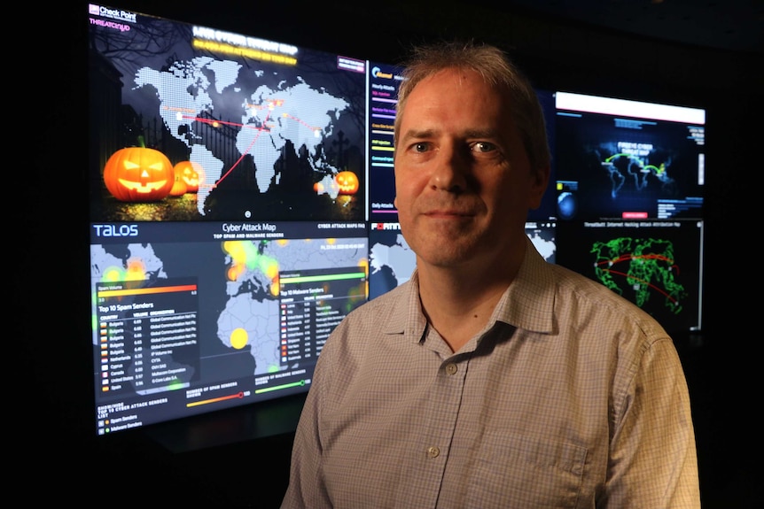 Associate Professor Paul Haskell-Dowland stands in front of screens showing cyber criminal activity around the world.