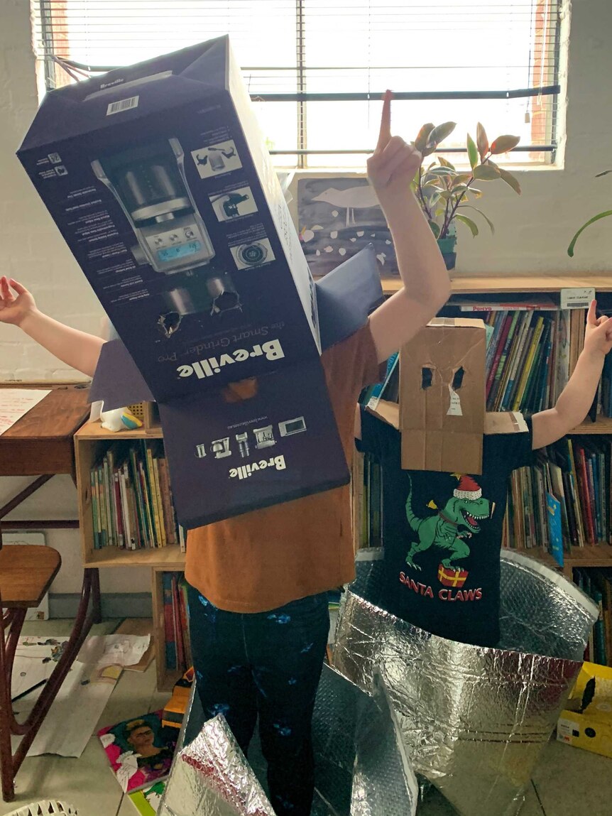 Two children stand with cardboard boxes over their heads, with eye holes cut out.