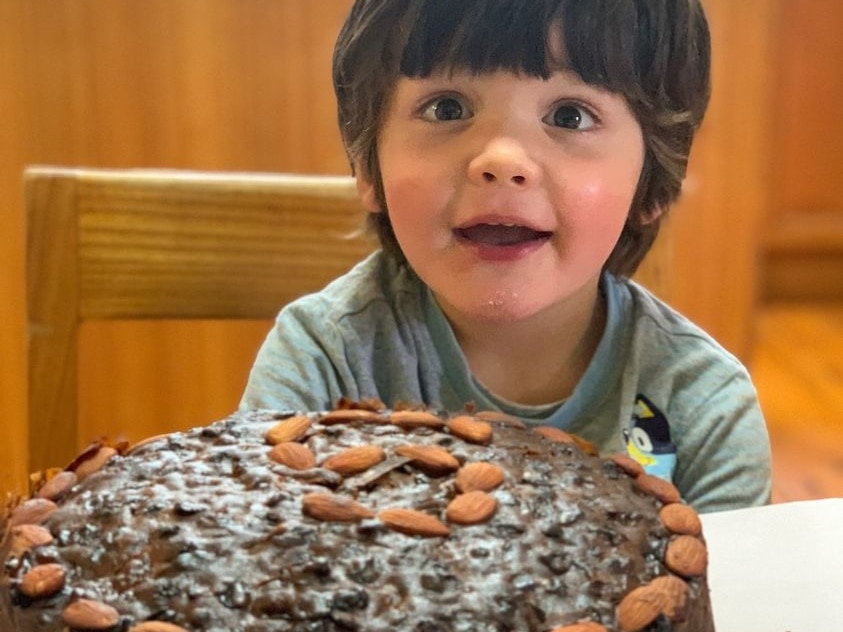 A boy with brown hair sitting behind a fruit cake.