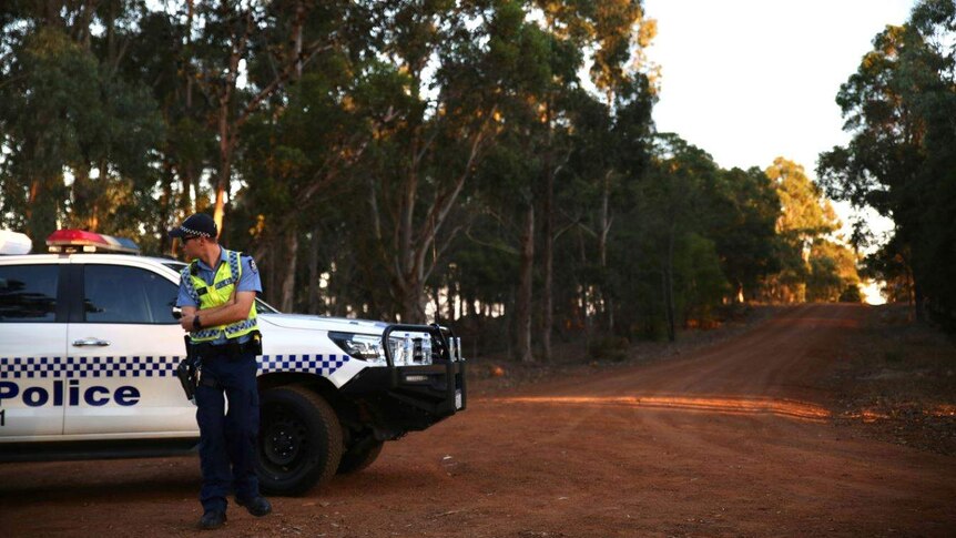 A police officer stands on an empty gravel road outside Margaret River.