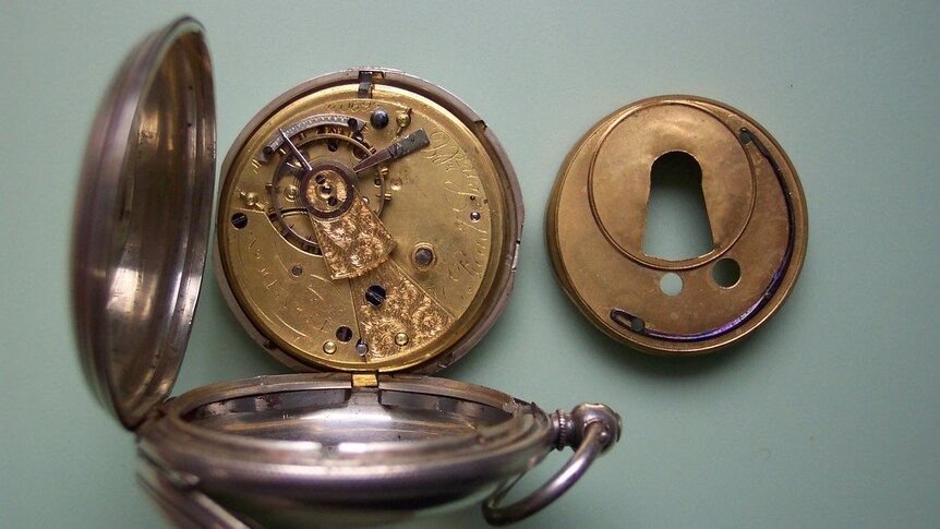 Image of the cogs and metal inside an old fob watch clock being pulled apart and repaired in workshop.