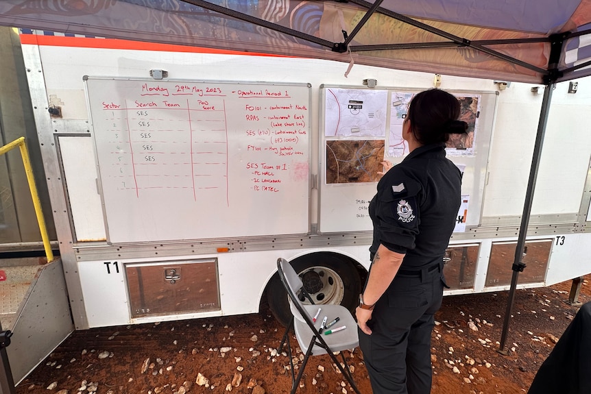 A female police officer looking at a whiteboard with photos. 