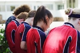 Several young children wearing red and blue shirts site on a wall in a courtyard.