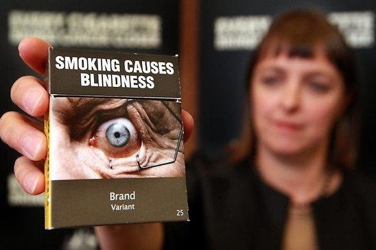 Nicola Roxon holds up a plain packaging pack of cigarettes.