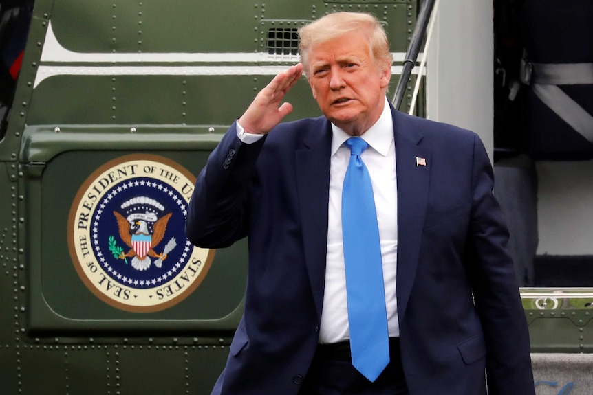 Donald Trump saluting while standing in front of the Marine One chopper