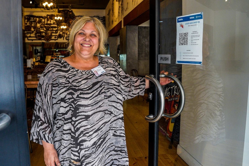 A woman stands in a doorway holding the door handle smiling.