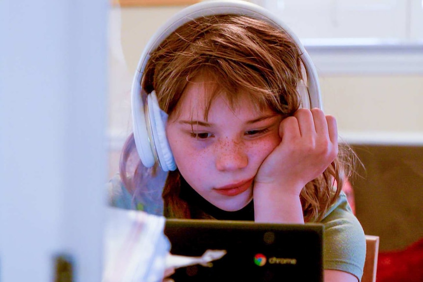 A little red heard girl wearing white headphones stares at a screen