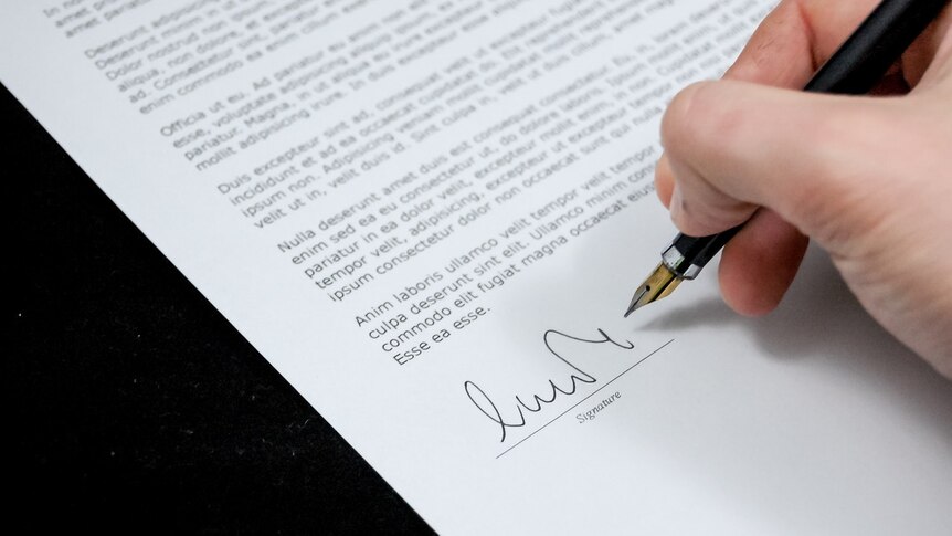 A hand holding a pen signing a legal document.
