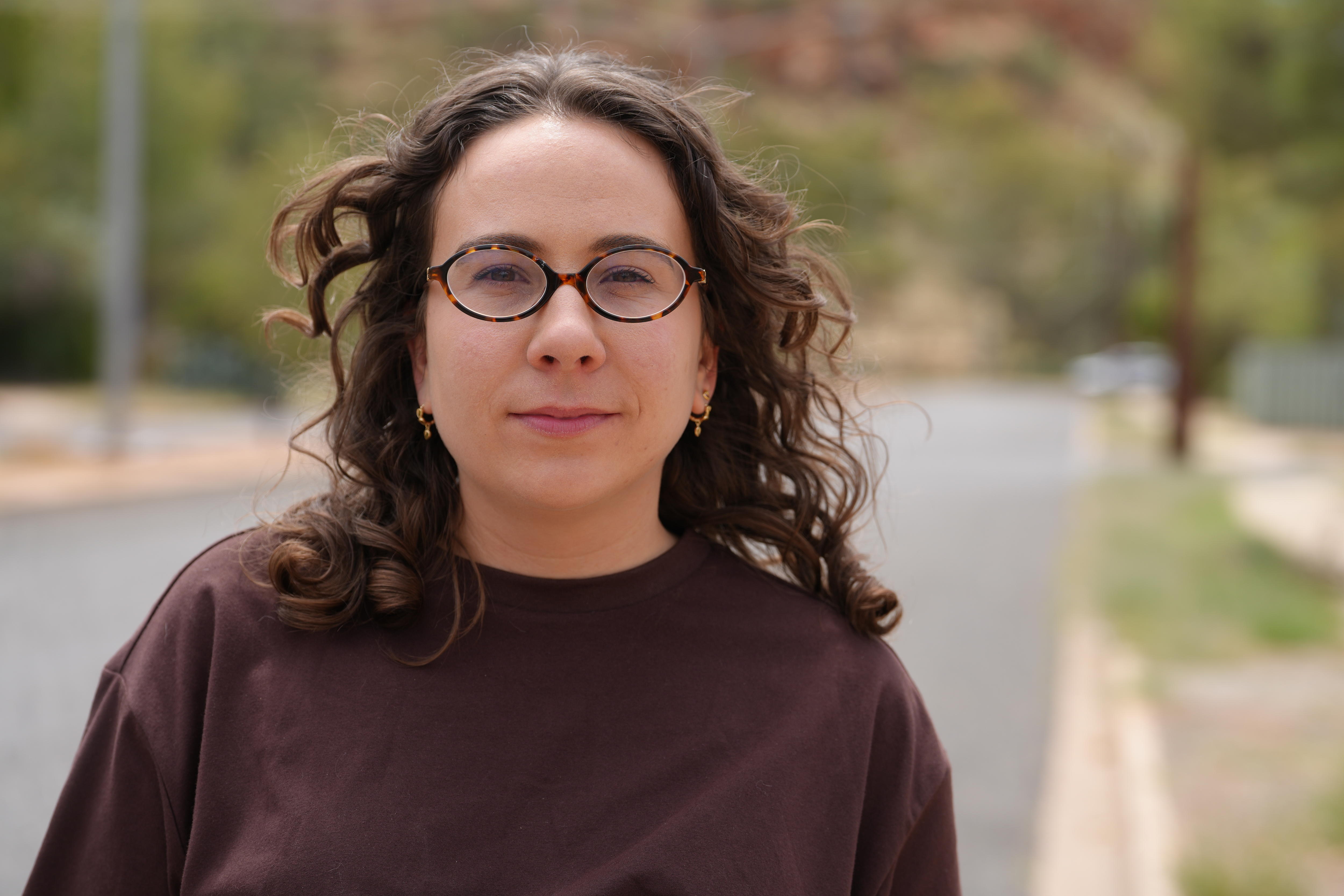 A women with short dark hair and glasses looks seriously at the camera.