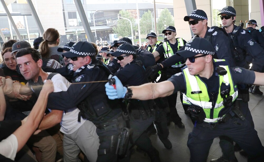 A group of police push back protesters and one officer sprays protesters with pepper spray outside the convention centre.