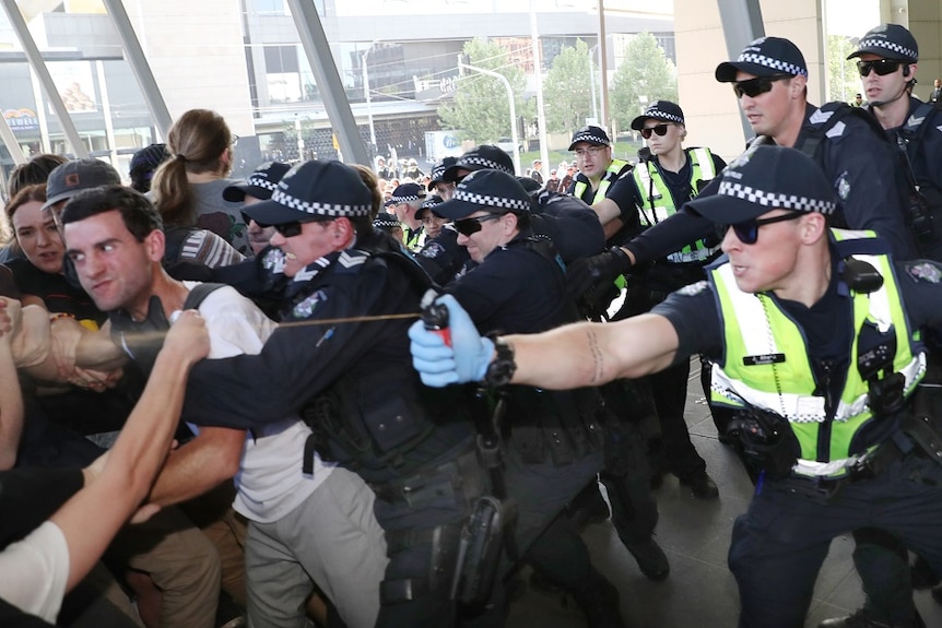 A group of police push back protesters and one officer sprays protesters with pepper spray outside the convention centre.