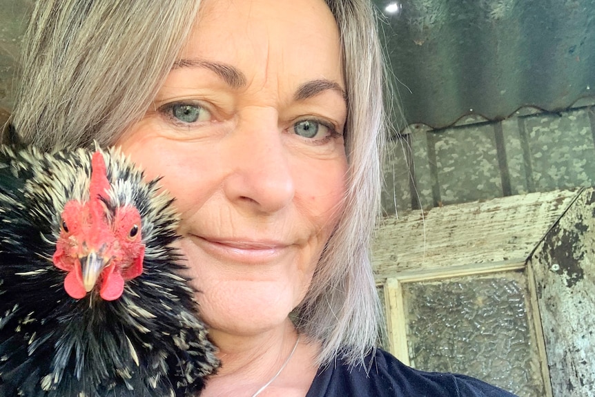 Mandy looks to the camera and smiles softly, with a black and white frizzle chicken on her shoulder.