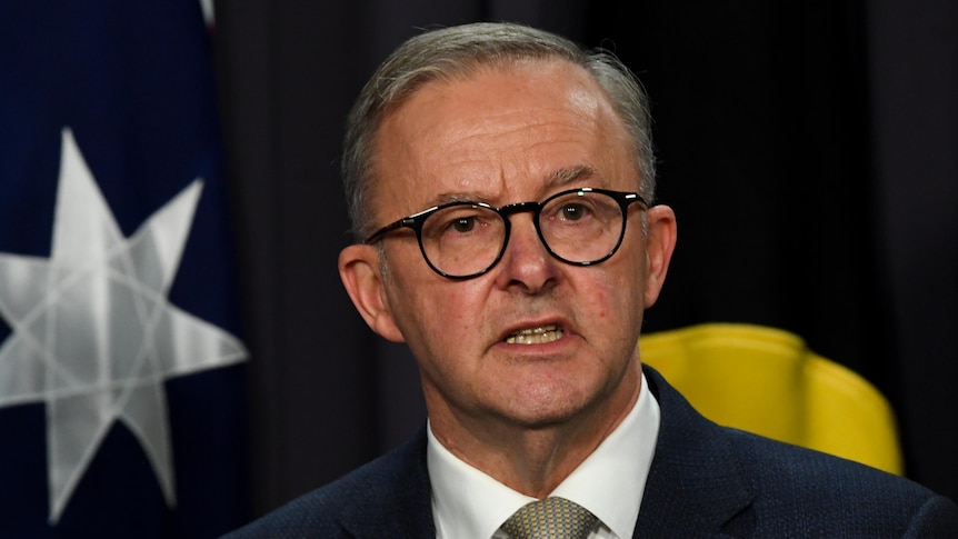 Anthony Albanese speaking in front of the Australian and Aboriginal flags.