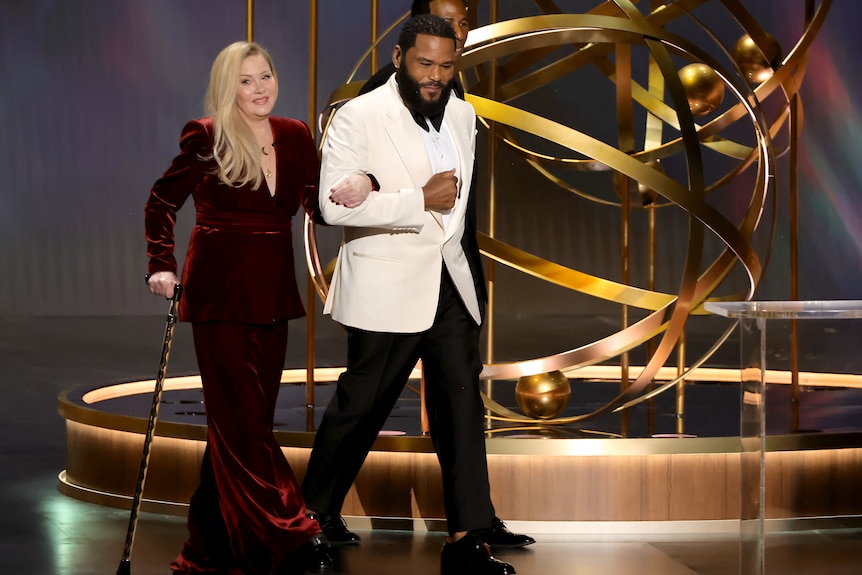 Christina Applegate walking onto the Emmy Awards stage using a cane for support.