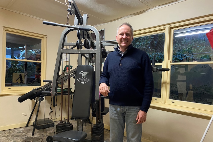 Nathan Doble stand next to his home gym, for a story about alternatives to gym memberships.