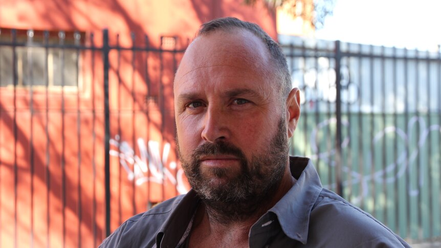 A man with a beard looking at the camera, serious, not smiling. 