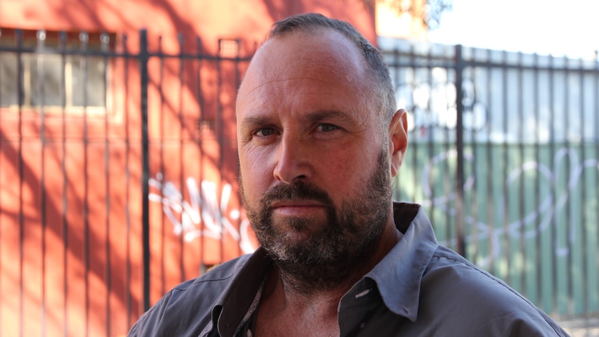 A man with a beard looking at the camera, serious, not smiling. 