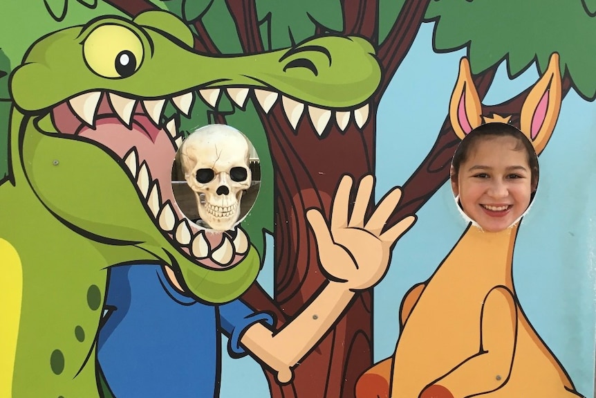 A skeleton and a young girl put their heads into holes, pretending to be a crocodile and kangaroo.