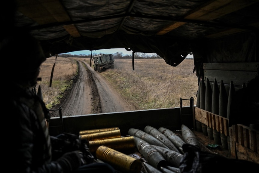 A shot taken through the back of a military truck. The bed of the truck is laid with artillery. 