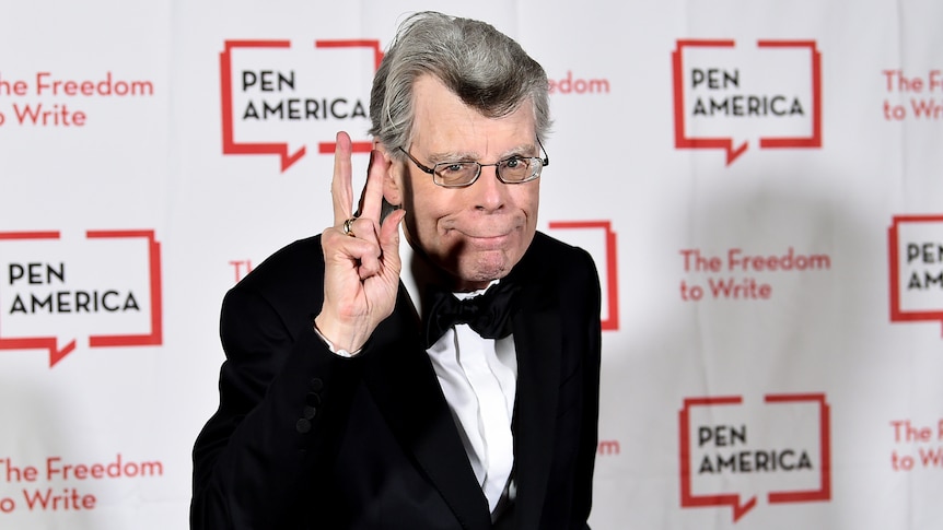 Author Stephen King poses for a photo wearing a tuxedo in front of a sign with the Pen America logo
