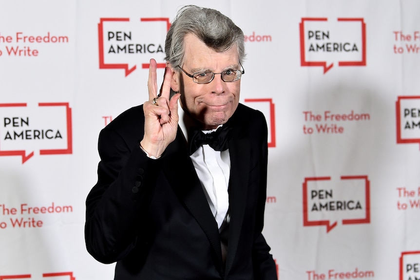 Author Stephen King poses for a photo wearing a tuxedo in front of a sign with the Pen America logo