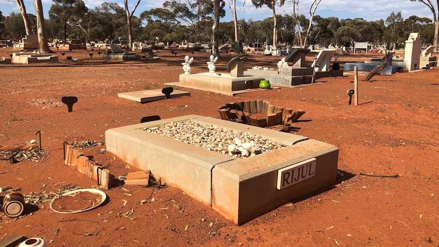 A close-up shot of an infant's grave in a red dirt cemetery.